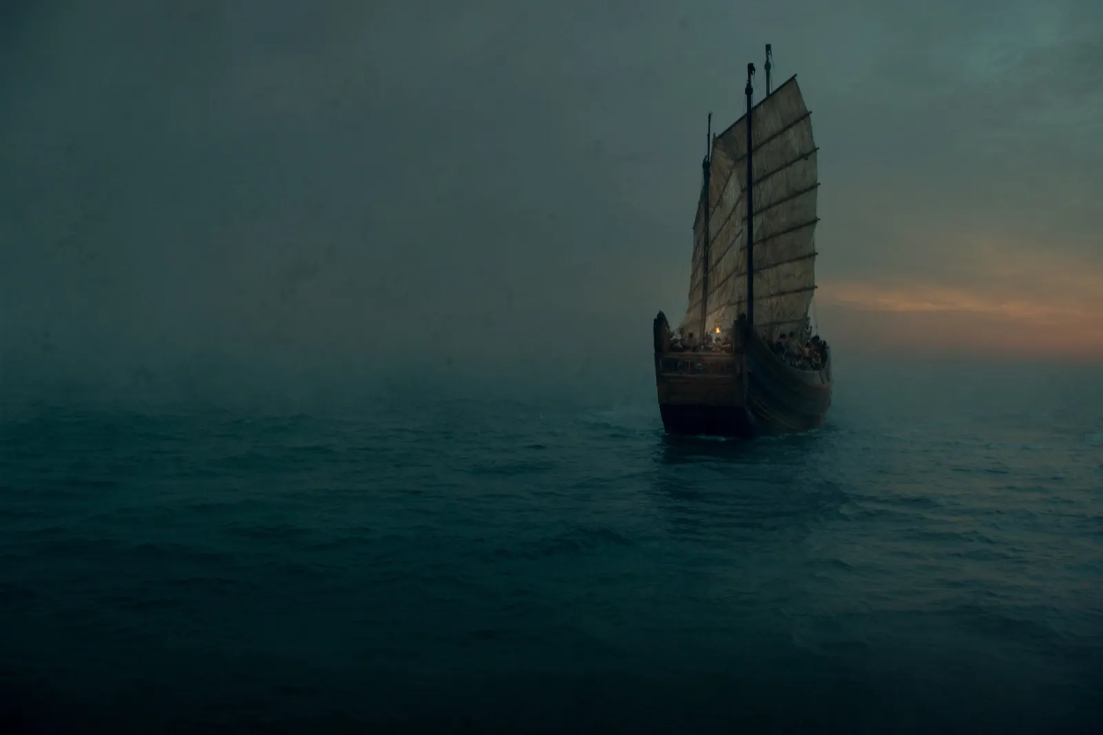 A Chinese junk under full sail crosses a misty, jade-grey sea at dusk, a thin band of warm light on the horizon — the long passage south.